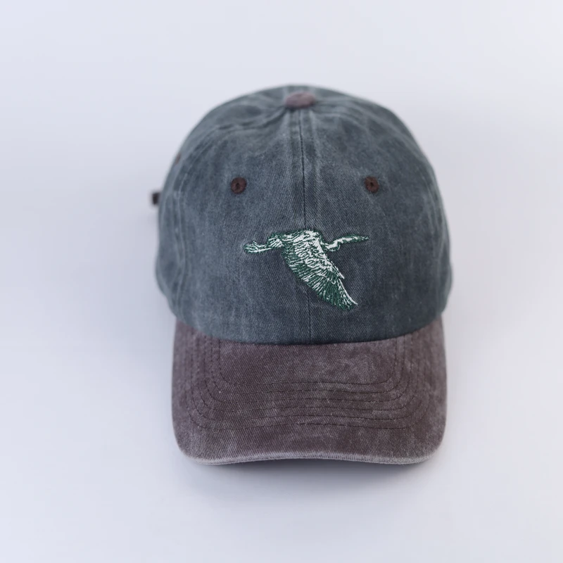 Front view of green washed-look dad cap with flying bird embroidery