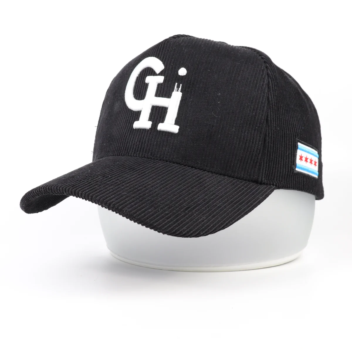 Three-quarter view of black corduroy baseball cap with large white front embroidery and side patch