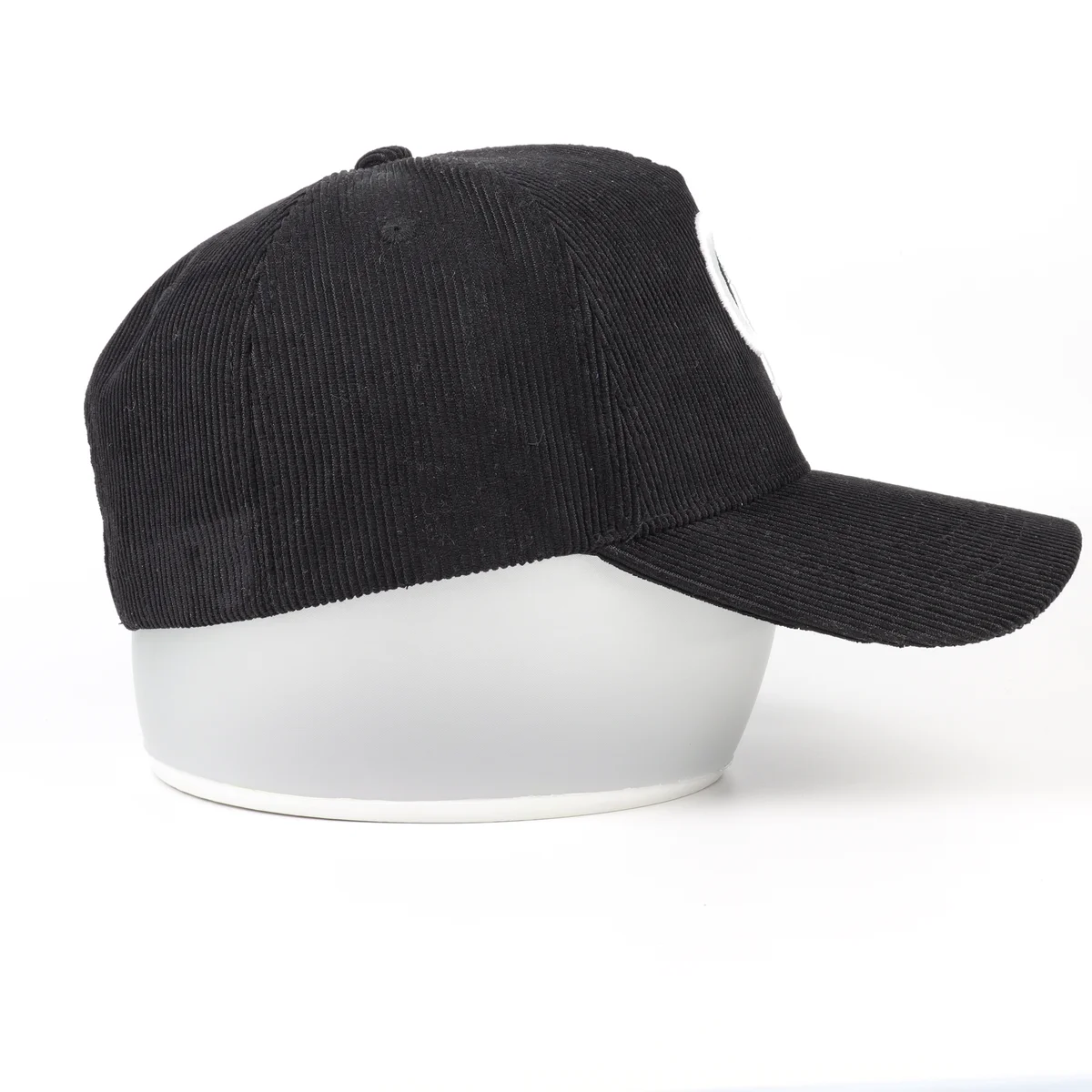 Side profile of a black ribbed corduroy baseball cap showing the curved visor