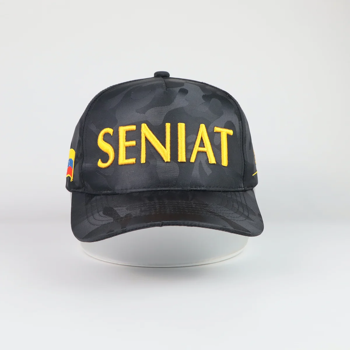 Front view of black tonal camouflage cap with yellow embroidered lettering