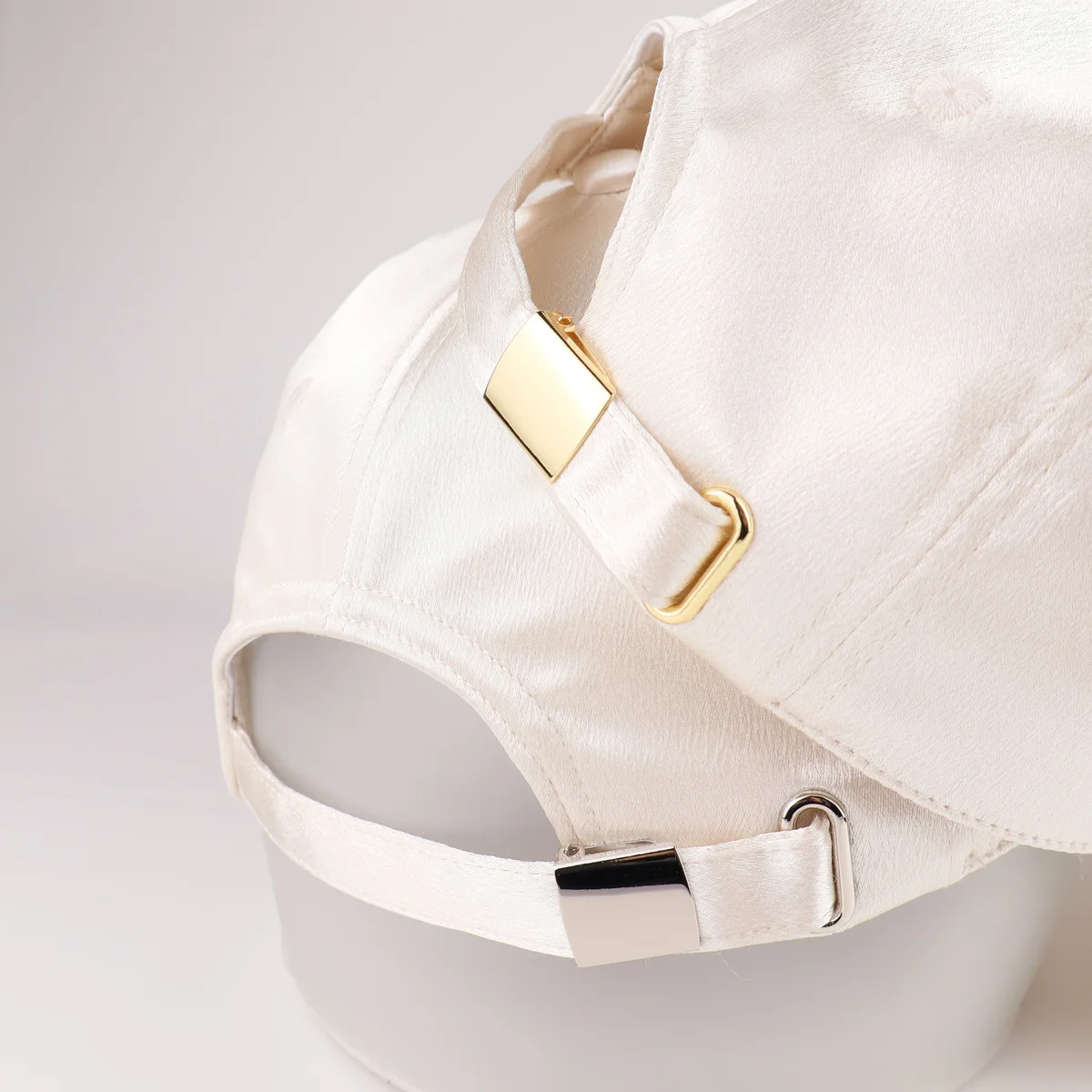 Close-up of gold-tone slider and ivory fabric strap on satin-look cap