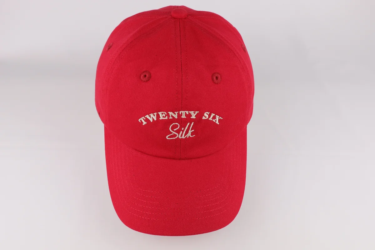 Front view of red curved-brim casual cap with small cream embroidered lettering